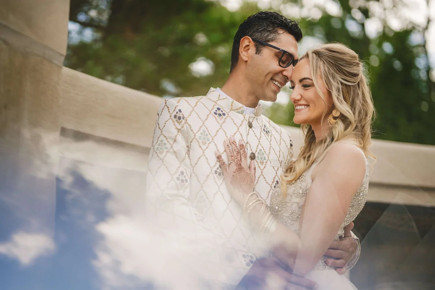 Bride and groom smiling and embracing outdoors on their wedding day, with the bride wearing henna designs for the special occasion.