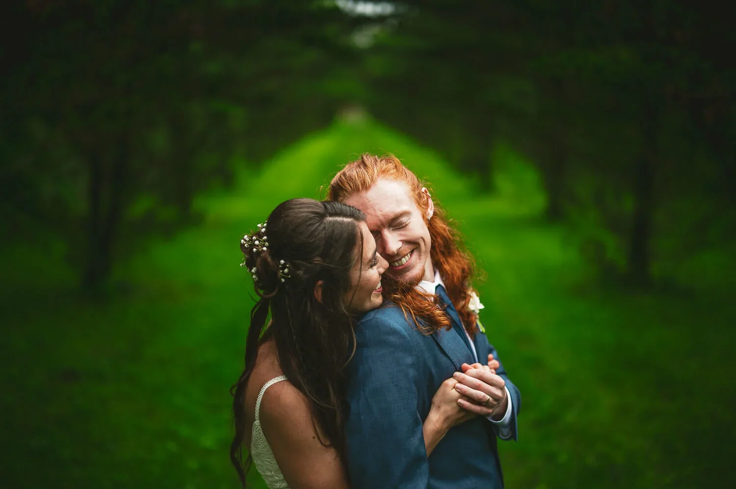 Wedding couple holding each other outside with a backdrop of lush greenery during their portrait session.
