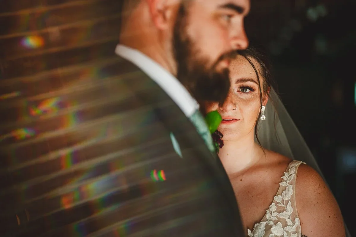 Groom in a suit looking ahead in the blurred foreground, with the bride in focus during their wedding portraits.