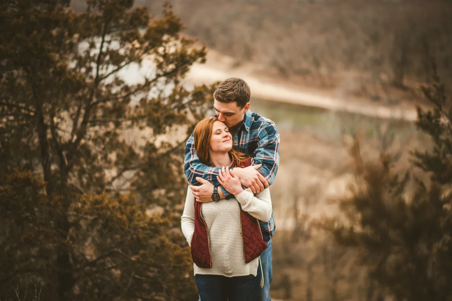 Fall engagement portrait of a couple embracing outdoors surrounded by autumn foliage.