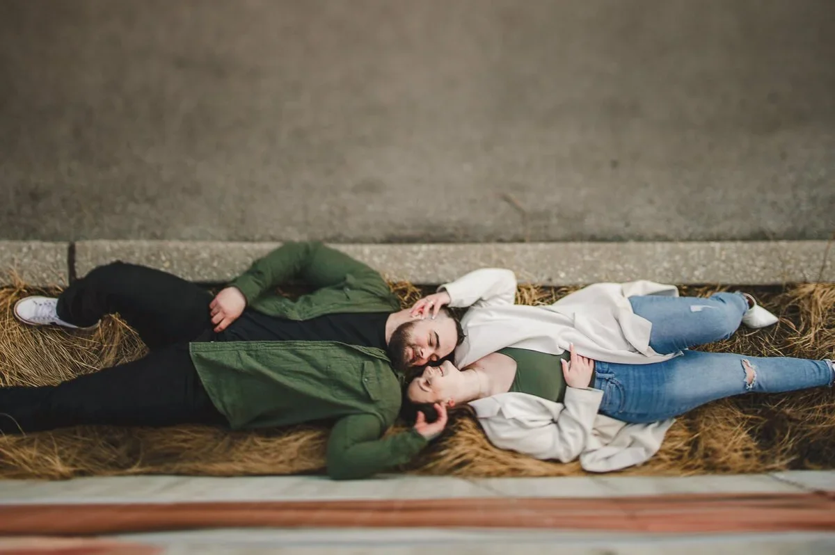 Overhead portrait of a couple laying side by side outdoors during their engagement photoshoot.