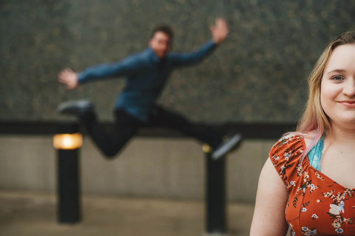Engagement portrait of a couple posing together while their partner playfully jumps in the background.
