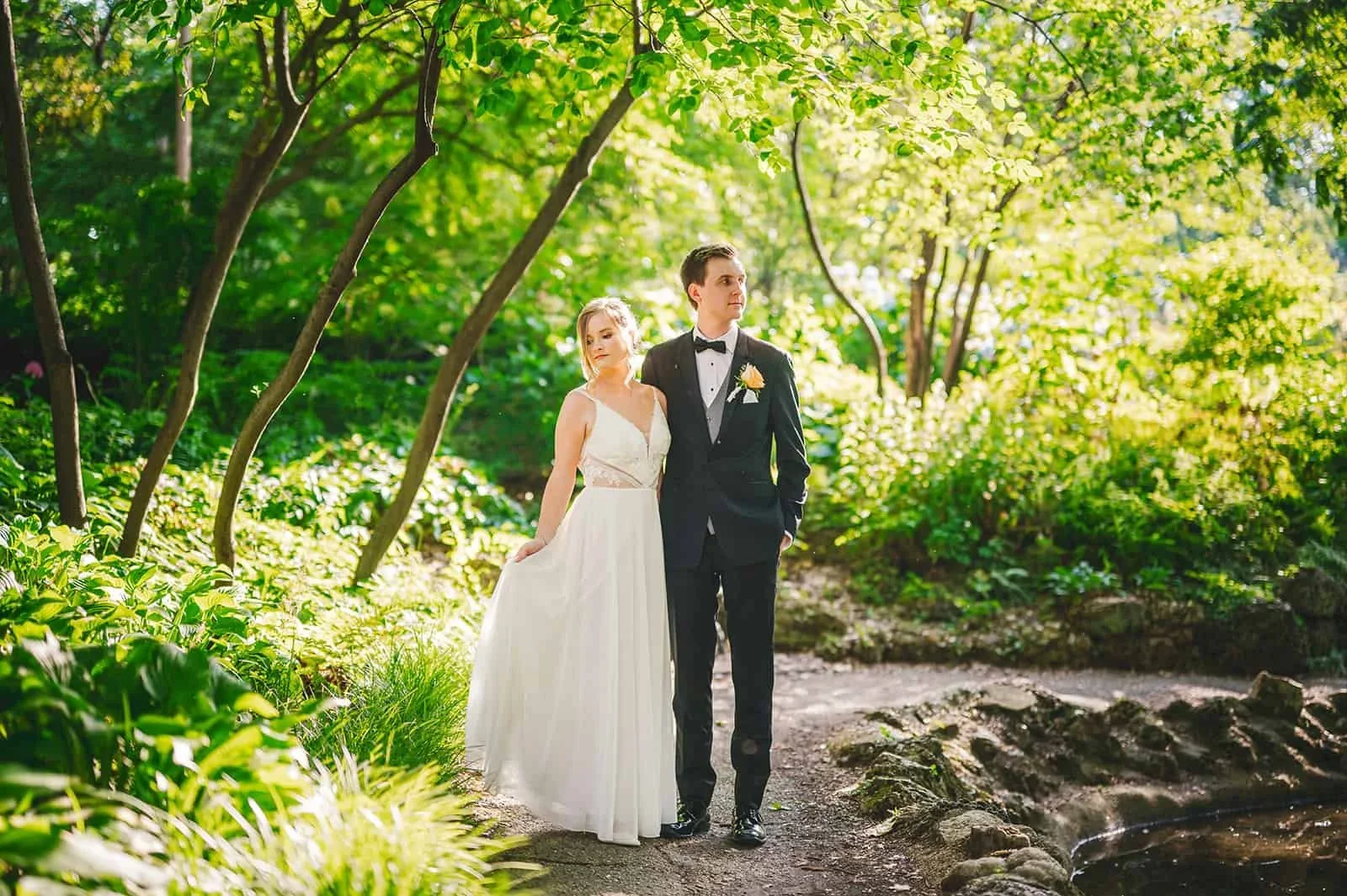 Couple posing for outdoor wedding portraits surrounded by lush green scenery on their wedding day.