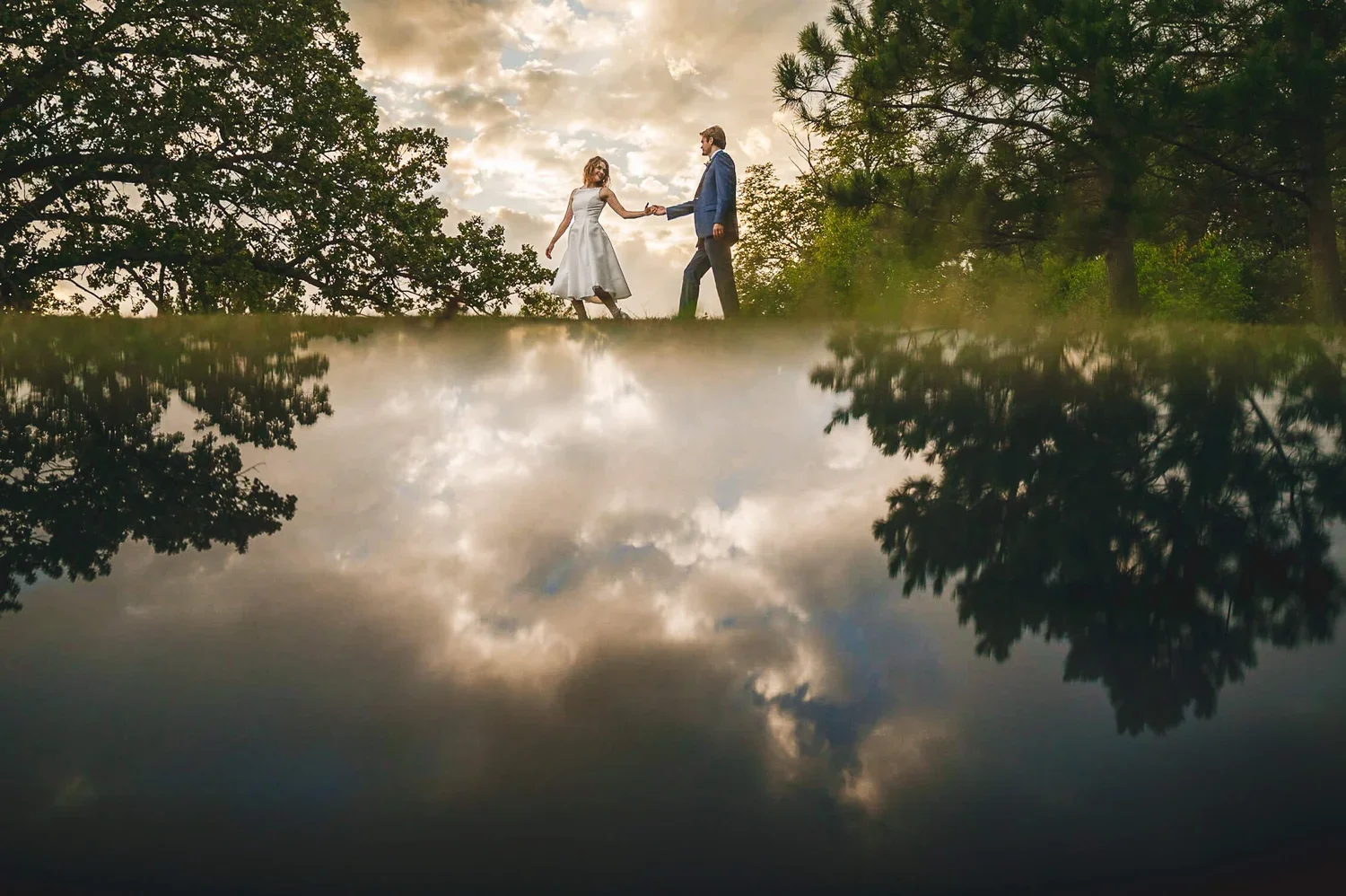 Wedding couple walking hand in hand with the sky reflected on the ground during their wedding day.