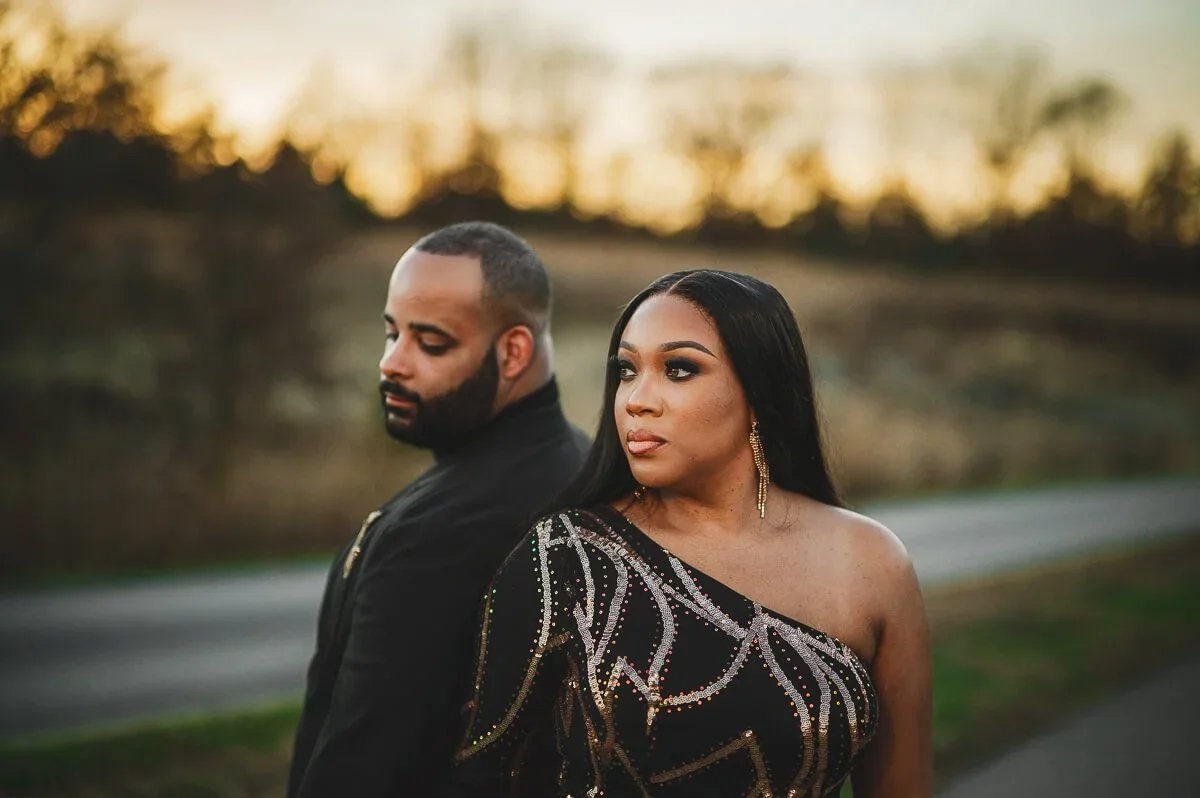 Couple standing side by side during an engagement photoshoot, looking left with serious expressions in warm golden hour light.