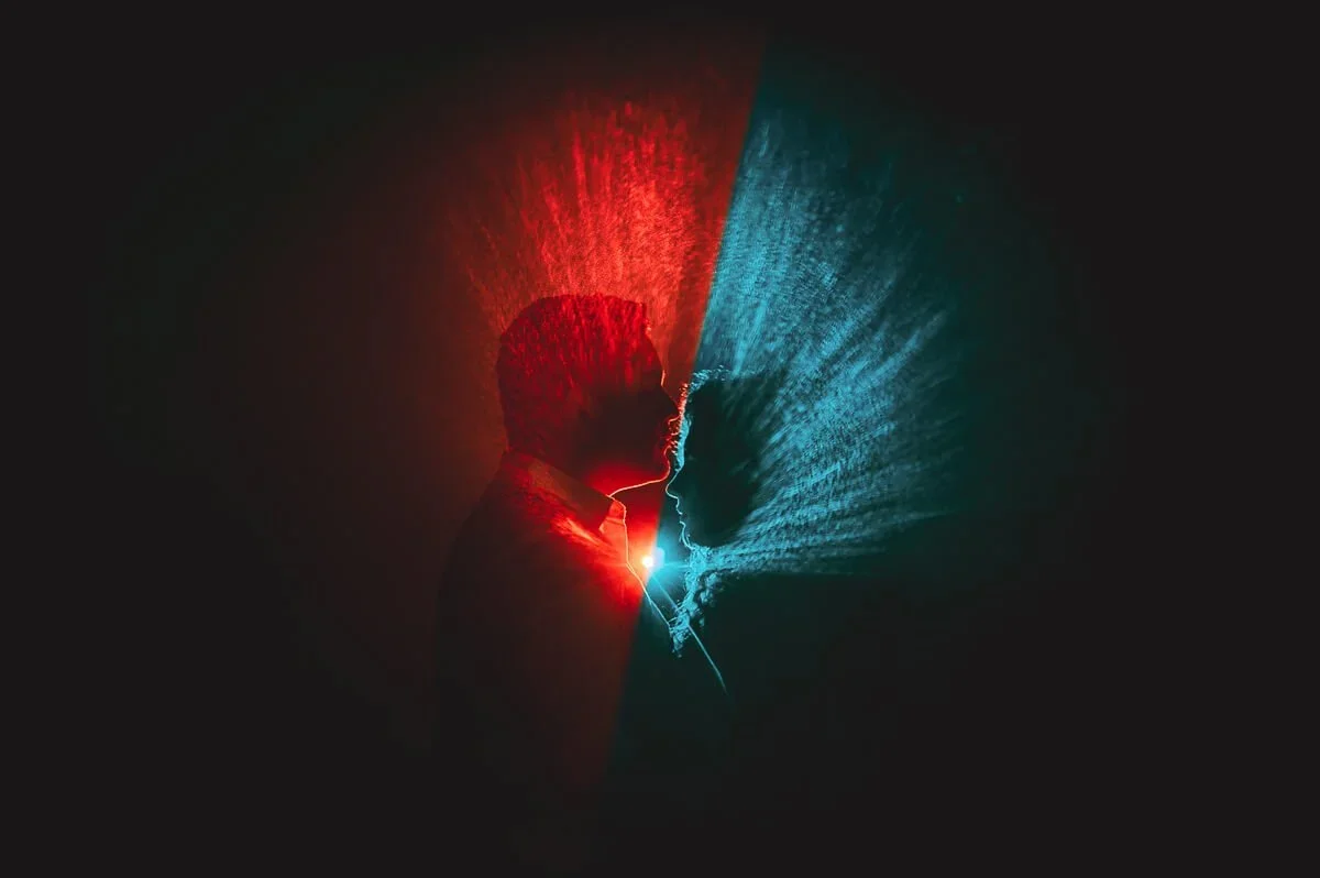 Silhouette portrait of a couple against a dark background illuminated with red and blue lighting.