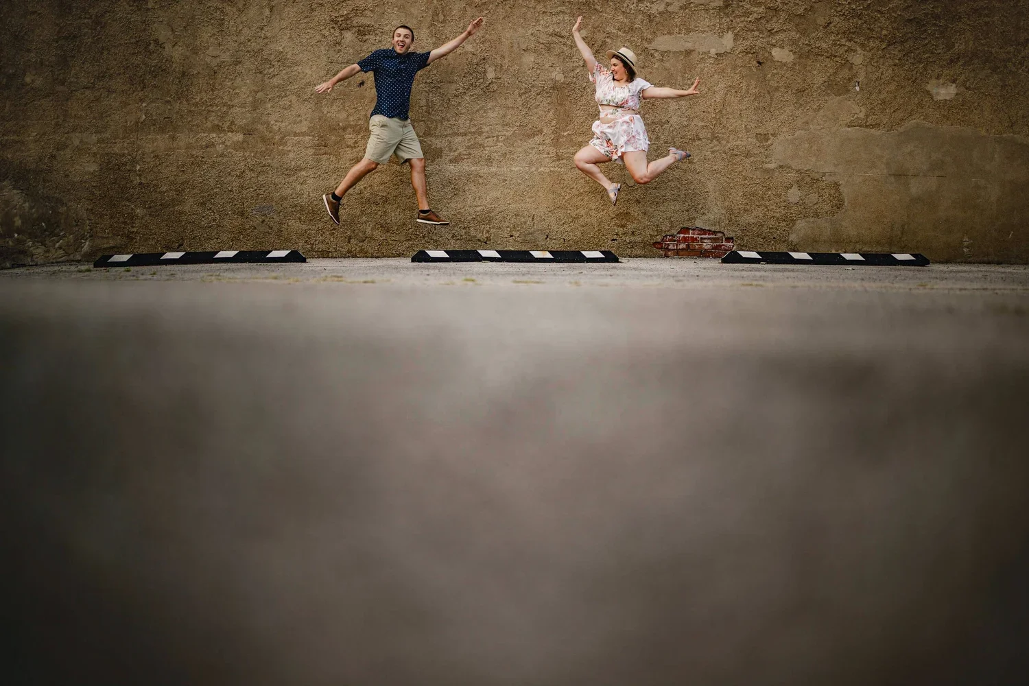 Couple jumping in midair during an engagement photoshoot with a wall as the background.