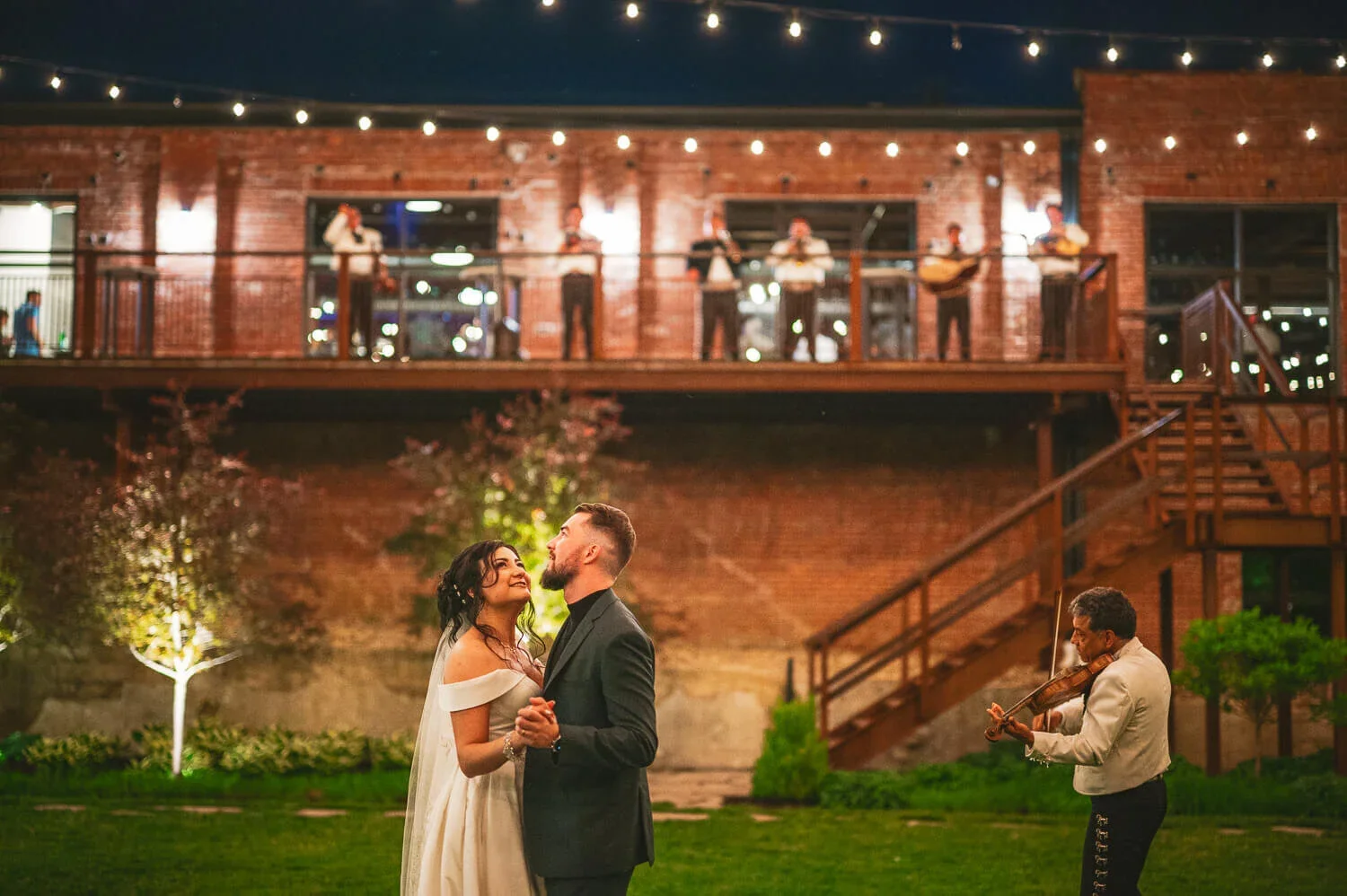 Bride and groom slow dancing during their evening wedding reception with a live band and soft lights surrounding them.