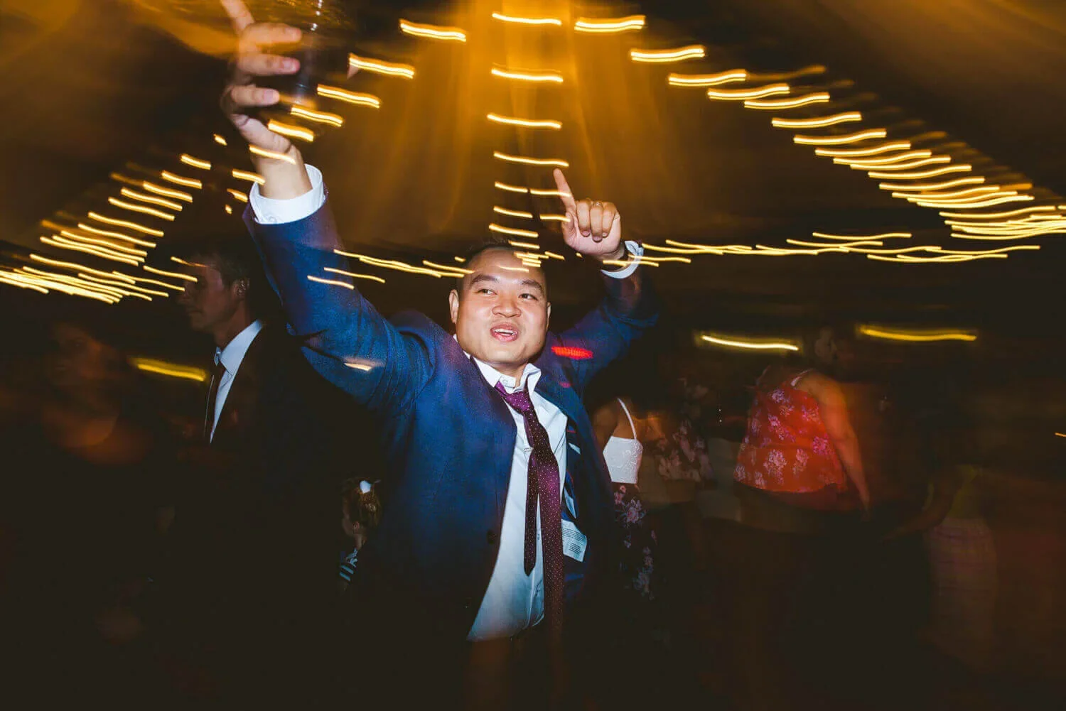 Wedding guest dancing at the reception with arms raised in the air, surrounded by blurred lights capturing movement.