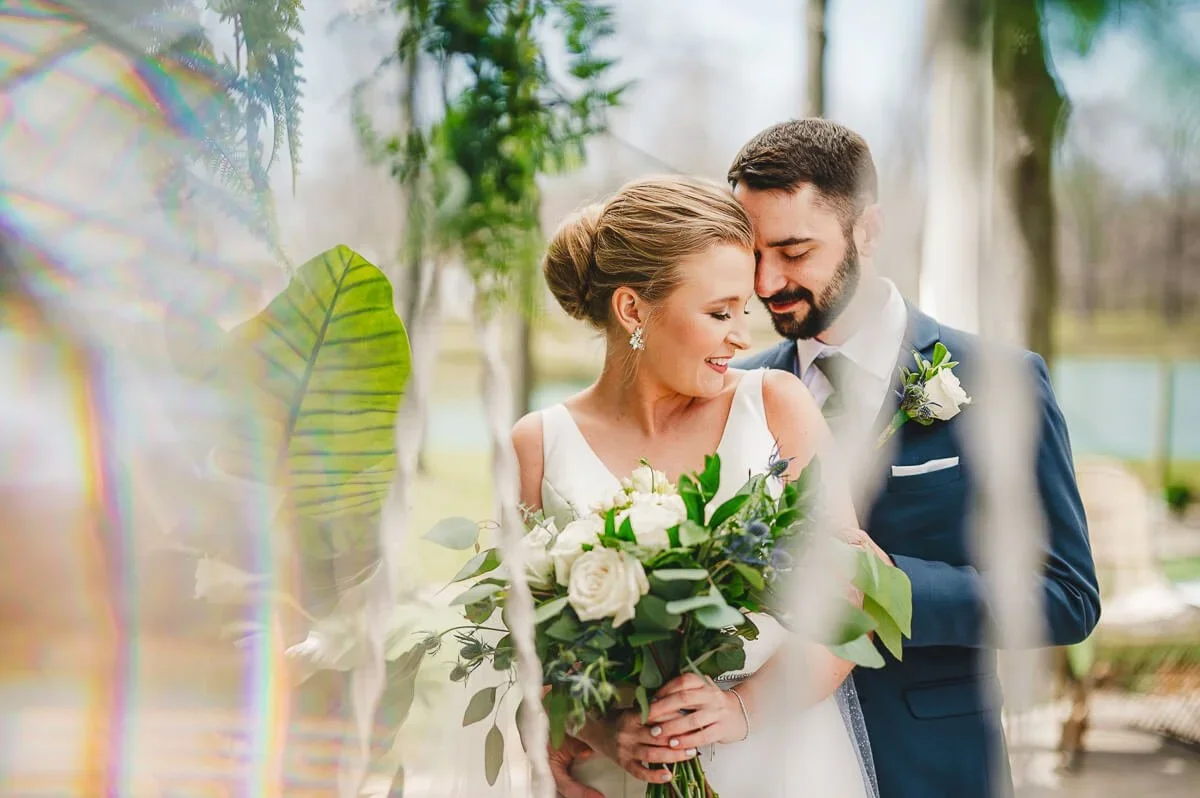 Wedding portrait of a bride and groom smiling on their wedding day, with the bride holding a bouquet of white flowers.