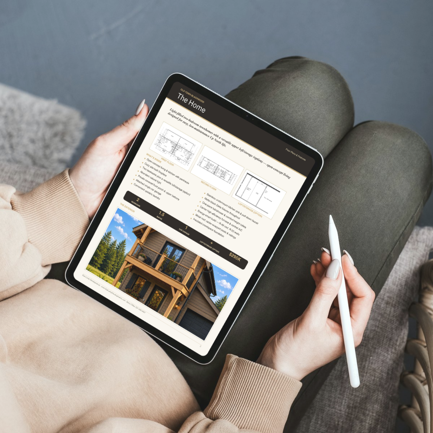 Person sitting on a couch using a tablet with architectural home listing, holding a stylus, wearing a beige sweatshirt, with green pants and a gray carpeted floor nearby.