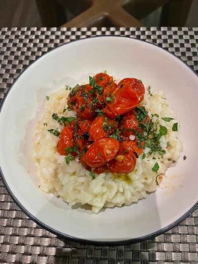 Creamy risotto topped with cherry tomatoes, basil, and olive oil in a white bowl
