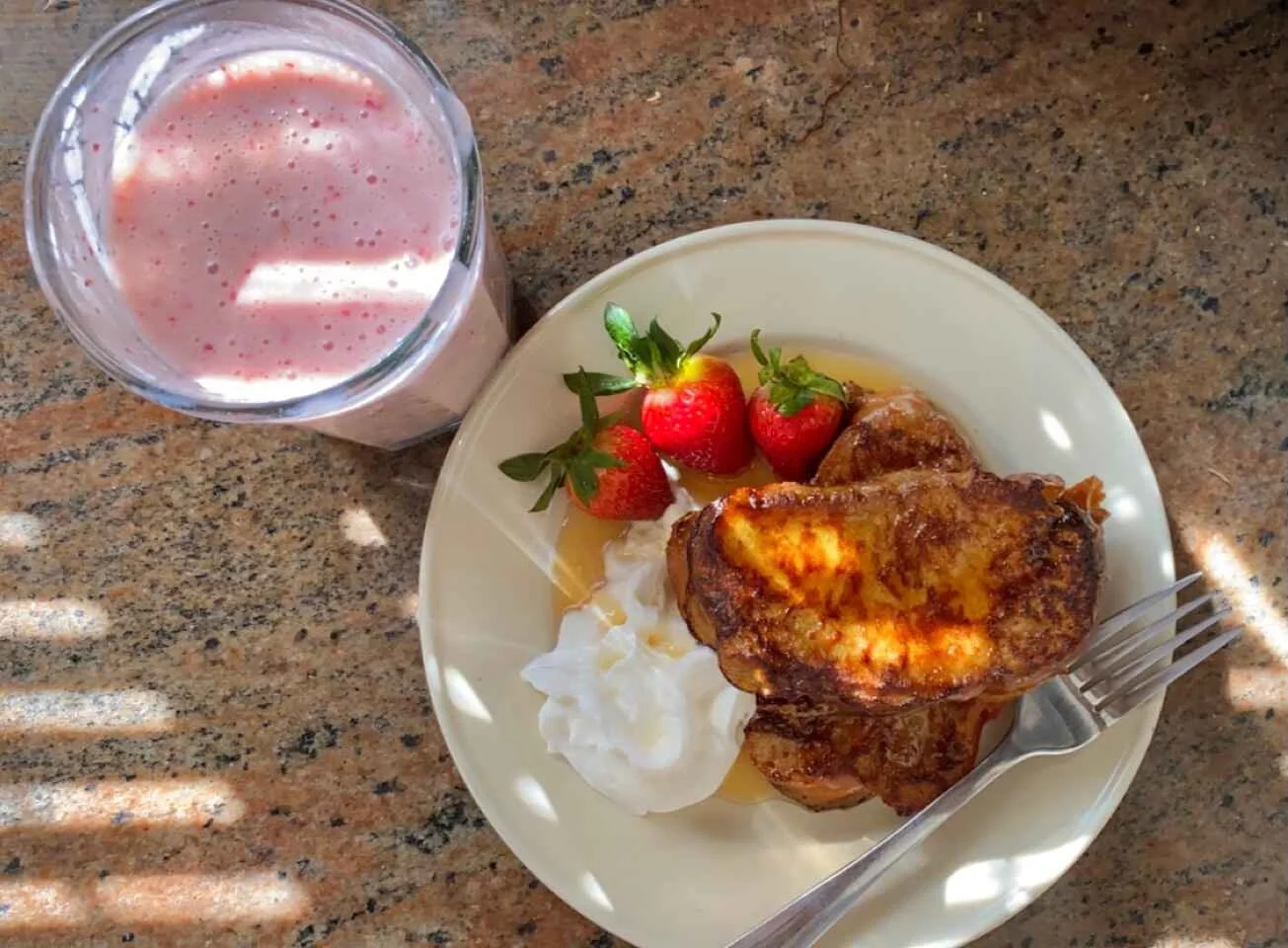 French toast with strawberries, whipped cream, and maple syrup served with a strawberry smoothie
