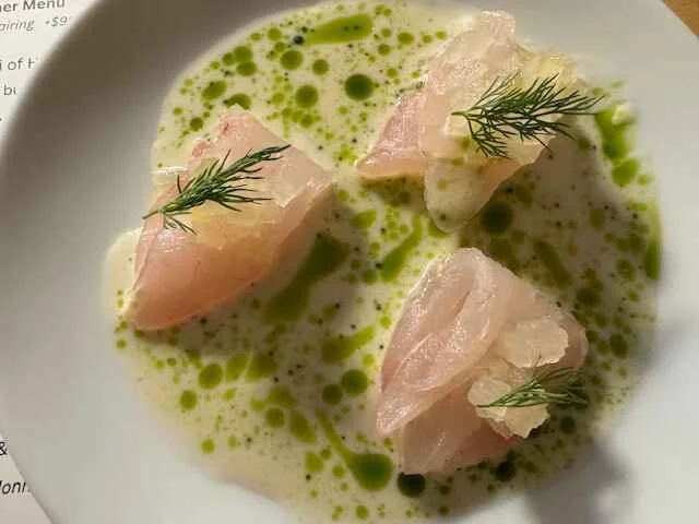 Delicate white fish sashimi with herb garnish and green oil on a white plate