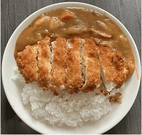 Japanese katsu curry with breaded chicken, white rice, and rich brown sauce in a white bowl