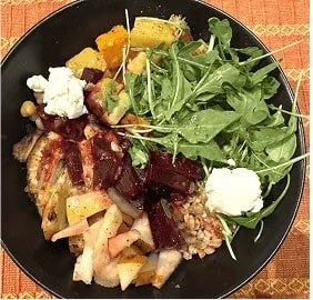 Grain bowl with arugula, roasted beets, goat cheese, chickpeas, squash, apples, and farro on a black plate