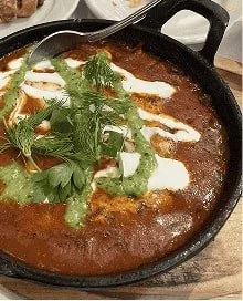 Shakshuka curry dish topped with herbs and drizzled yogurt served in a black skillet