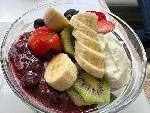Colorful fruit bowl with sliced banana, kiwi, strawberries, blueberries, and yogurt in a glass bowl