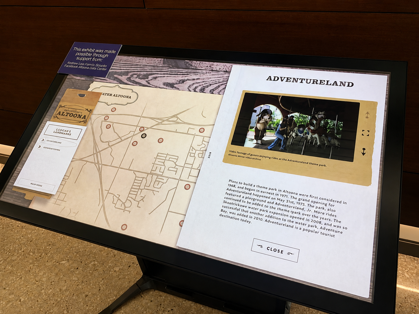 Information display about Adventureland theme park, including a map of Altoona, Pennsylvania, and a photo of guests riding the carousel with horse figures, with a sign mentioning support from Andrew Lee Family Scopio Facebook Altoona Data Center.