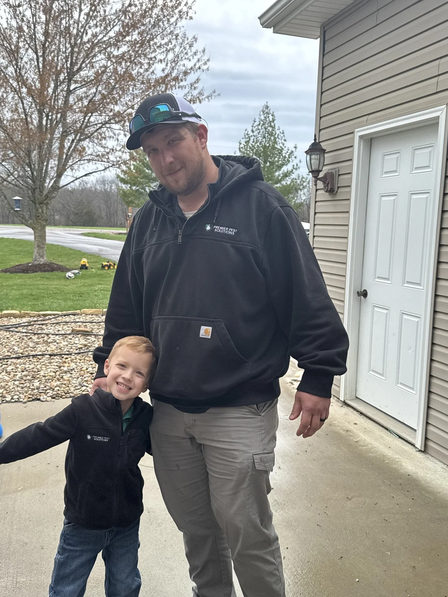 Brice, the owner of Premier Pest Solutions, wearing a Premier Pest Solutions Hoodie posing with his son. Brice is a family man and you can tell by his son's smile.
