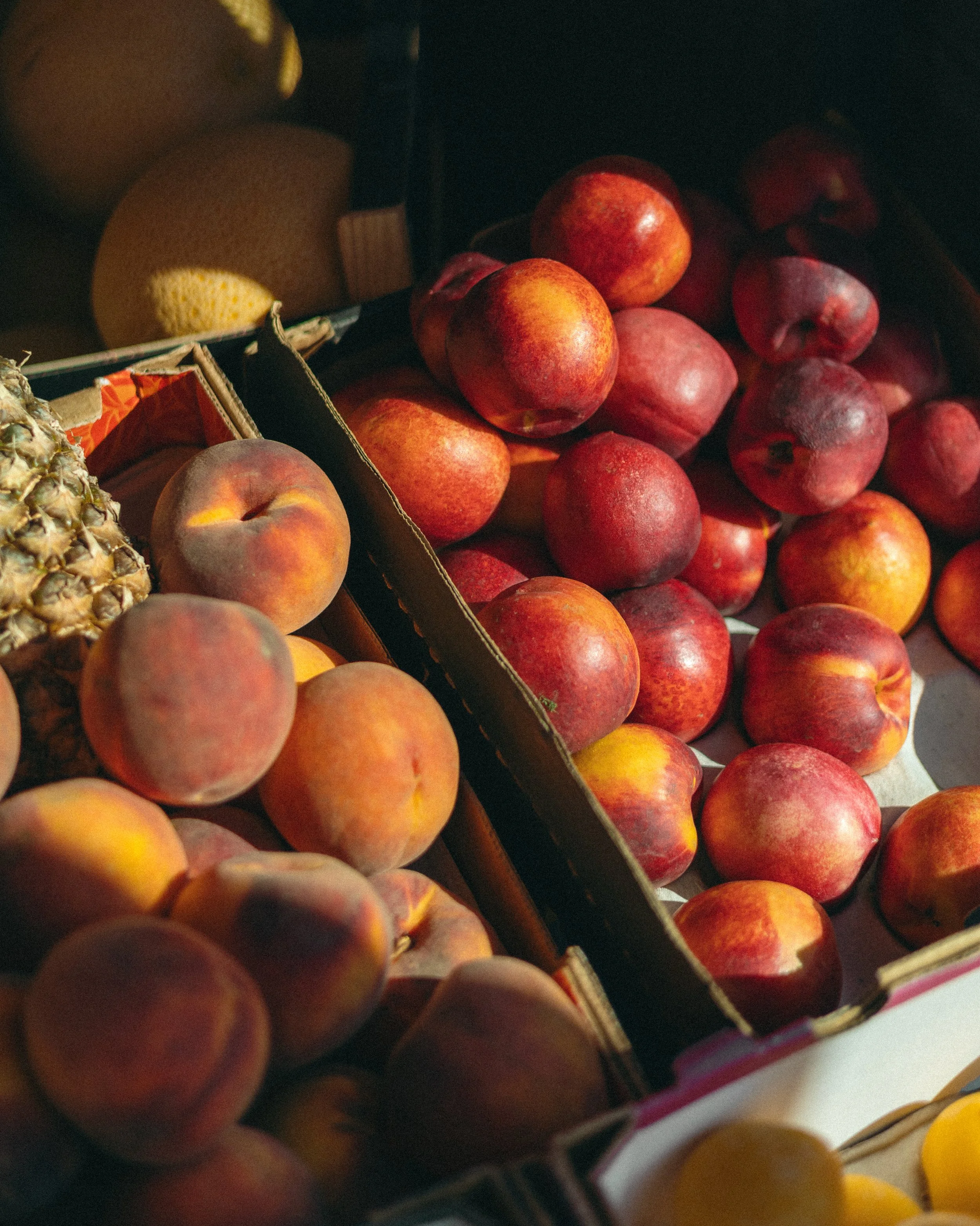 A cardboard box filled with red apples and a pineapple on the side.