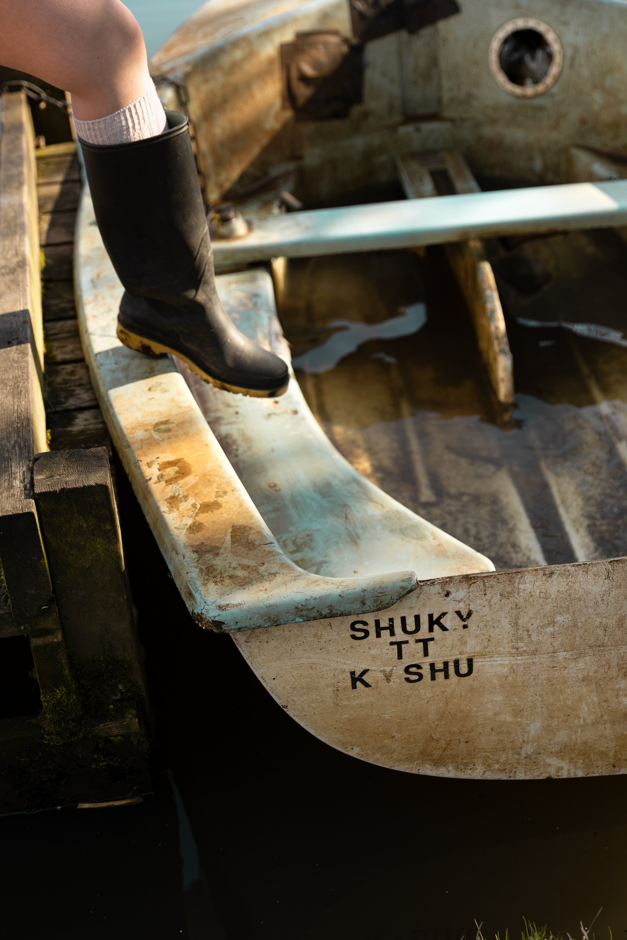 Close-up of an old, weathered rowboat floating on water with a person's foot inside wearing a black rubber boot.
