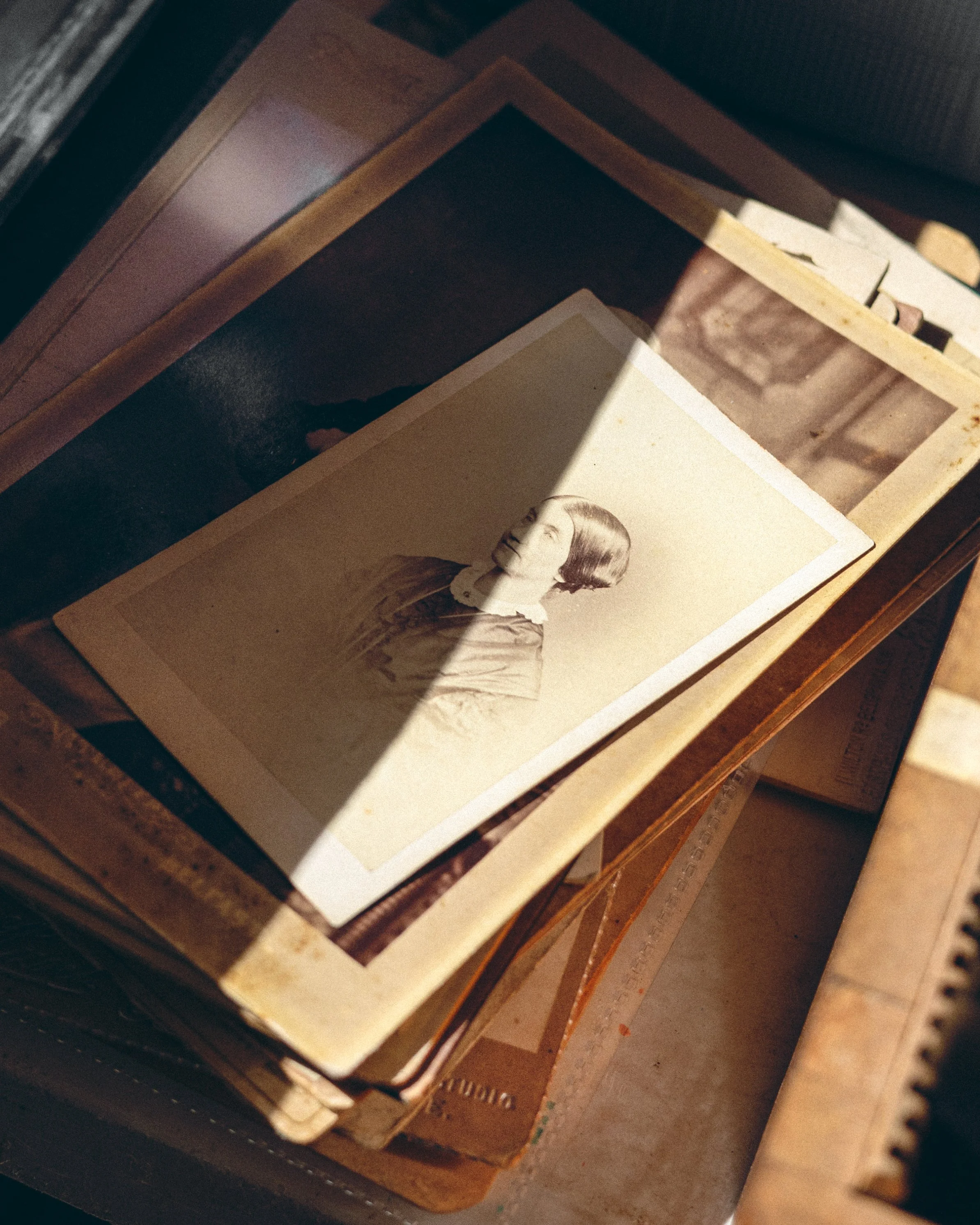 Old black-and-white photograph of a woman with a bob haircut on top of a stack of vintage photo albums or books.