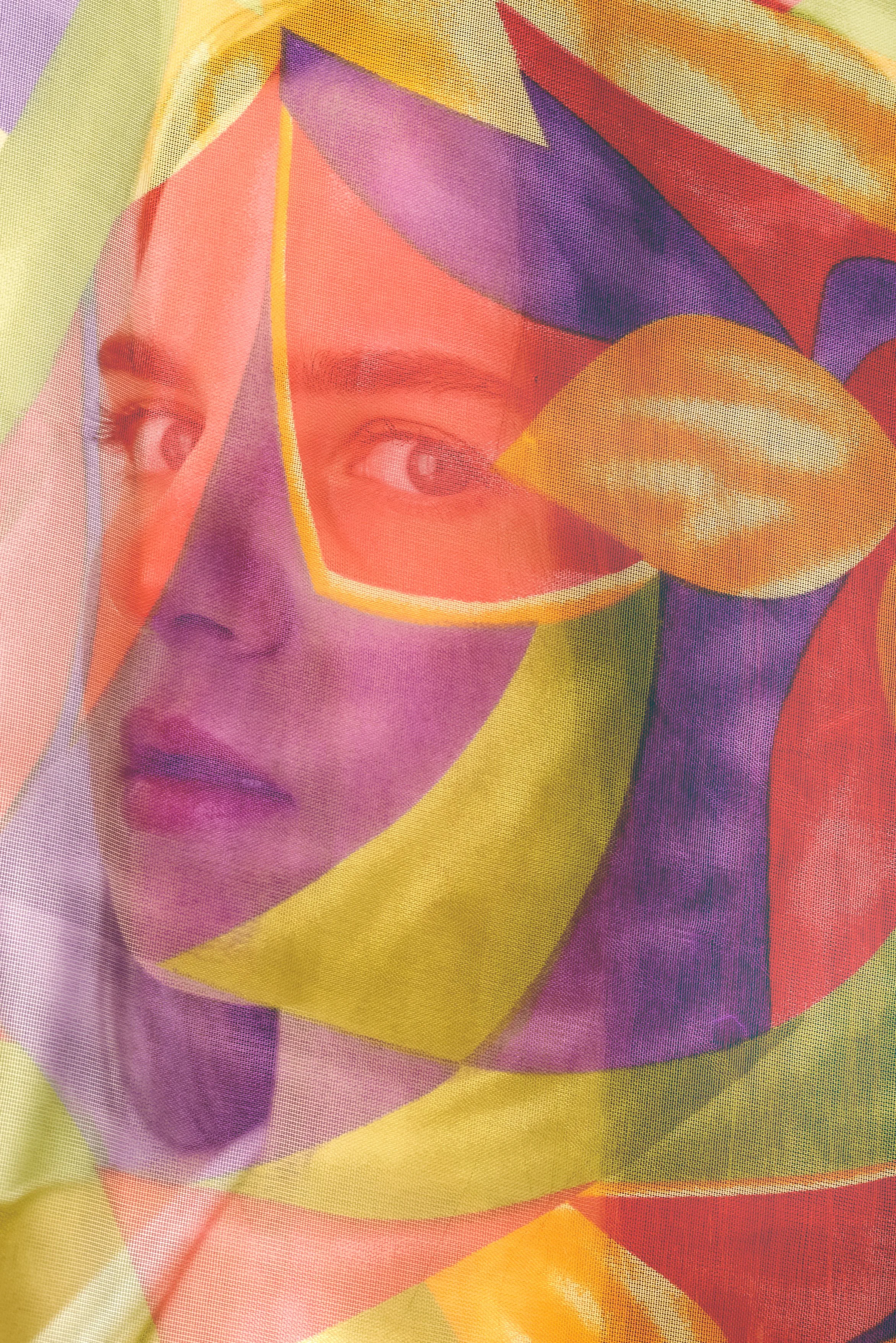 A woman's face is covered by multicolored, abstract geometric shapes in yellow, purple, red, and green.