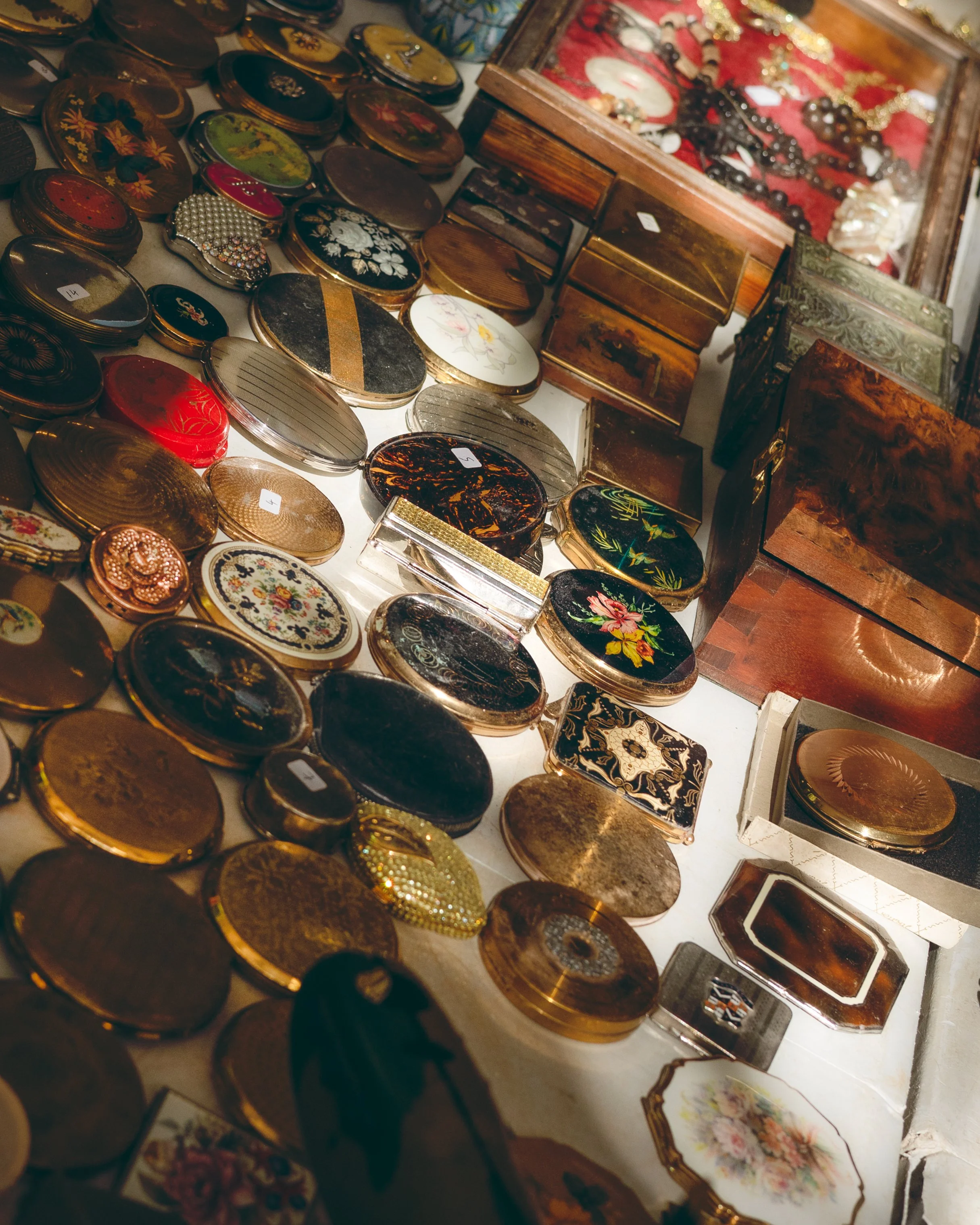 A collection of vintage jewelry boxes and decorative tins with floral and ornate designs displayed on a table.
