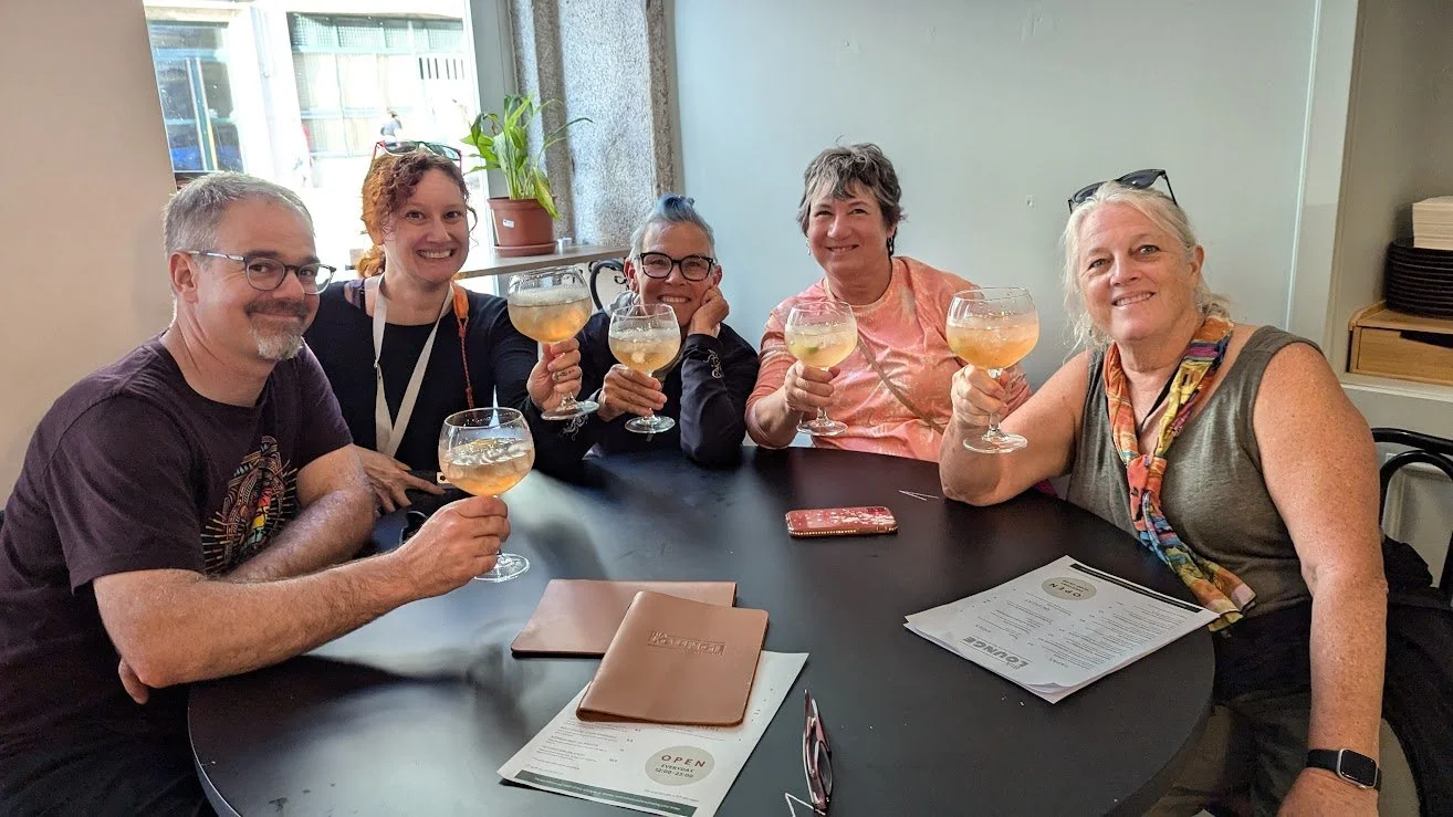 Six people sitting at a restaurant table, raising glasses filled with a light-colored beverage, smiling for the camera.