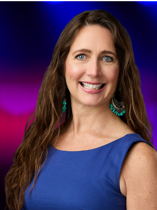 Photo of NSA Michigan President Robin Shear. She is smiling, has long wavy brown hair, and is wearing a sleeveless blue dress.