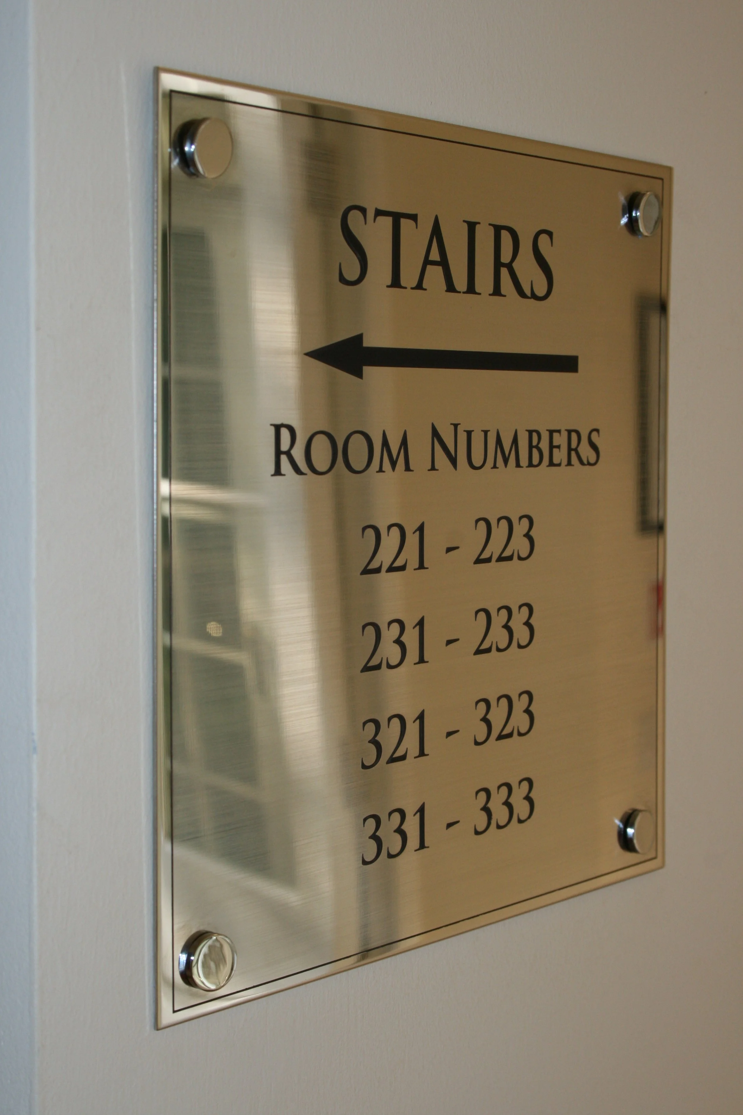 A hallway directory sign for rooms with numerical ranges, marked with an arrow pointing to the left, labeled 'STAIRS' in large black letters.