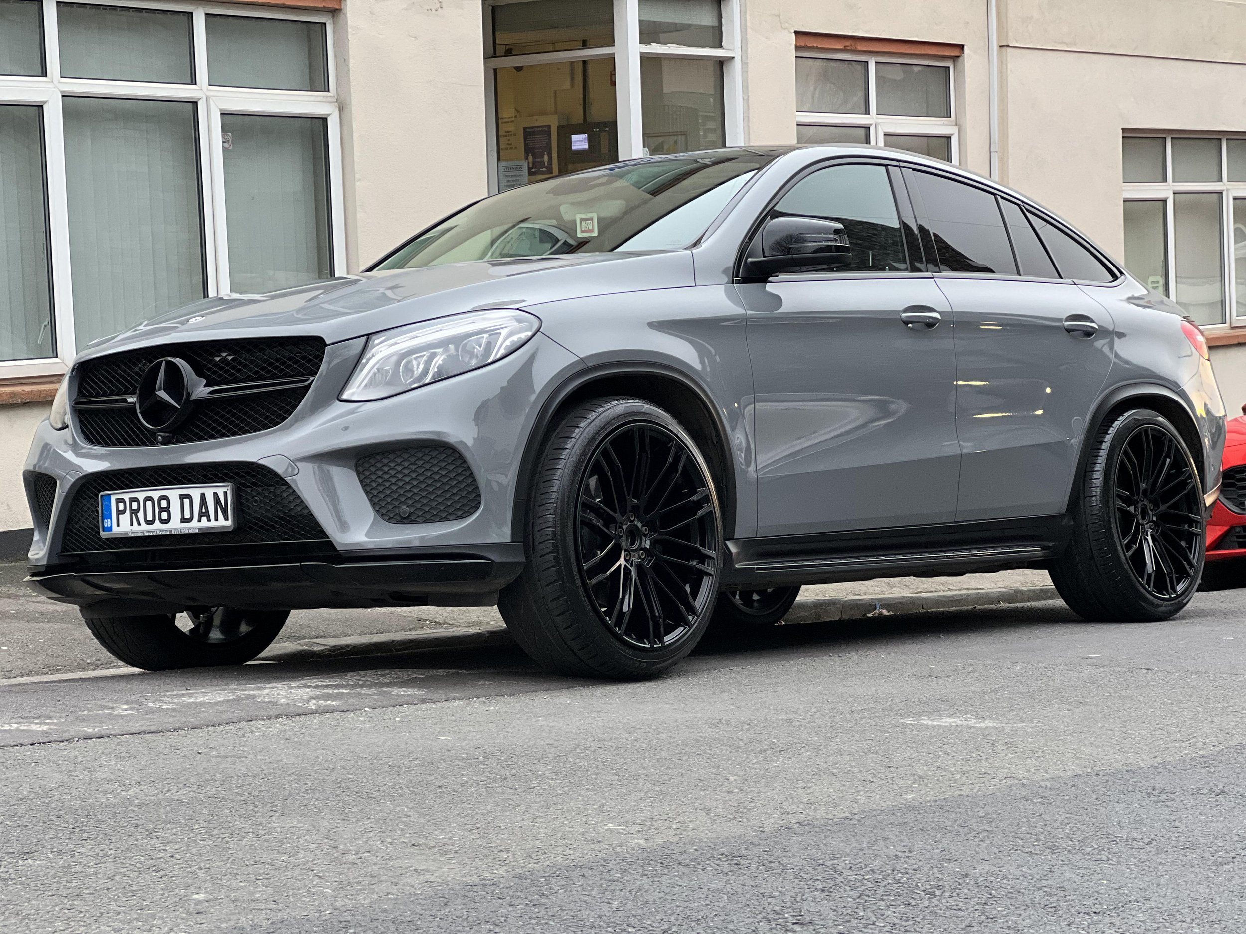 A silver Mercedes-Benz SUV parked on the street in front of a building with large windows.