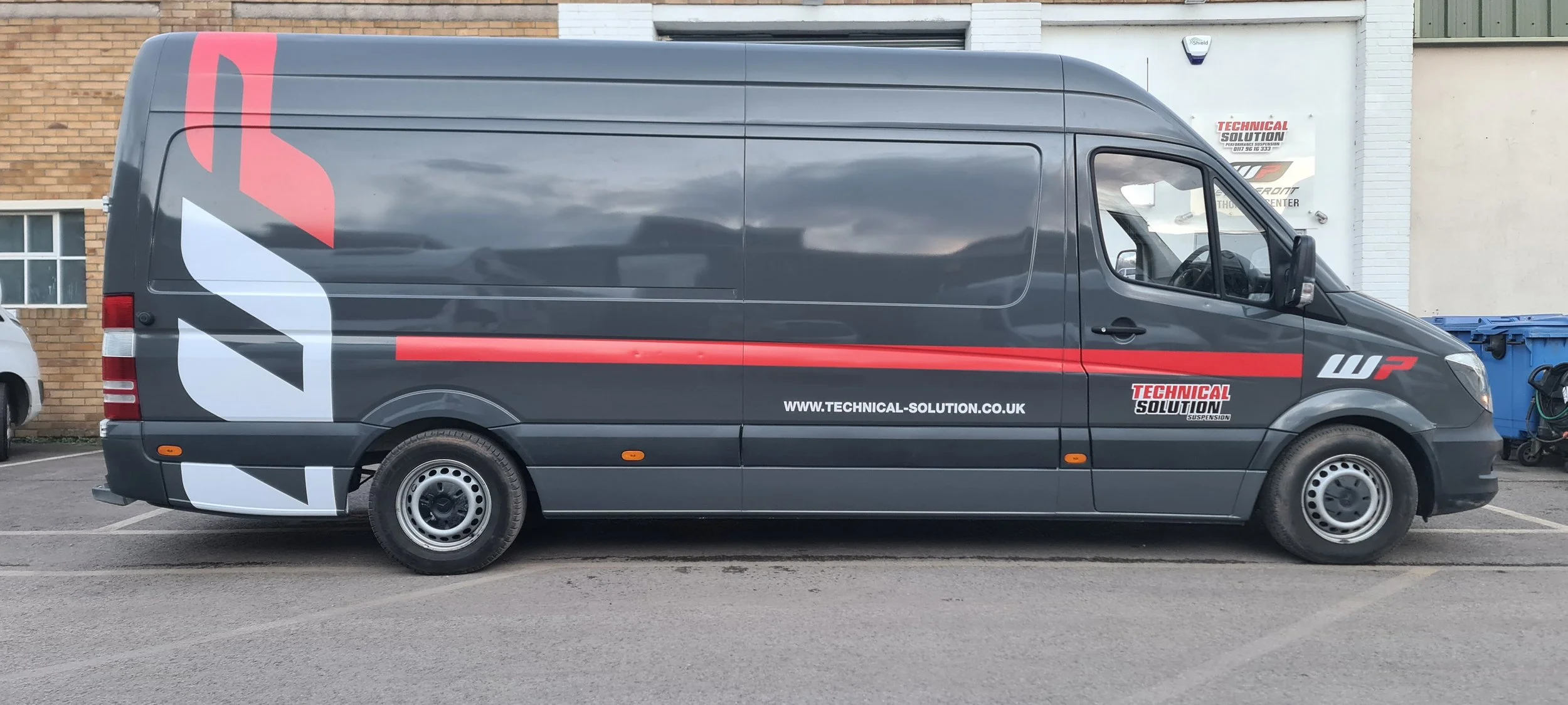 Gray commercial van with red, black, and white logo and text, parked in front of a brick and white building. Website URL www.technical-solution.co.uk is visible.