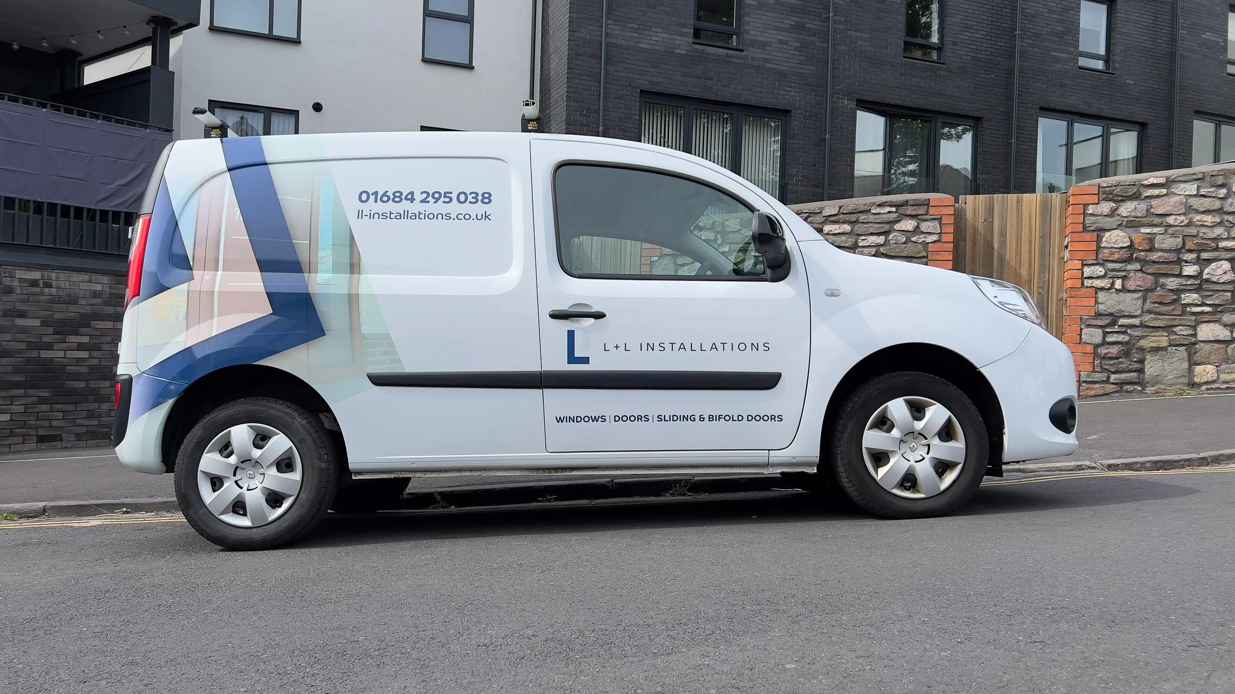 White work van parked on the street with company branding, including contact number and services such as windows, doors, sliding and bifold doors, in front of a modern residential building with brick, stone, and window details.