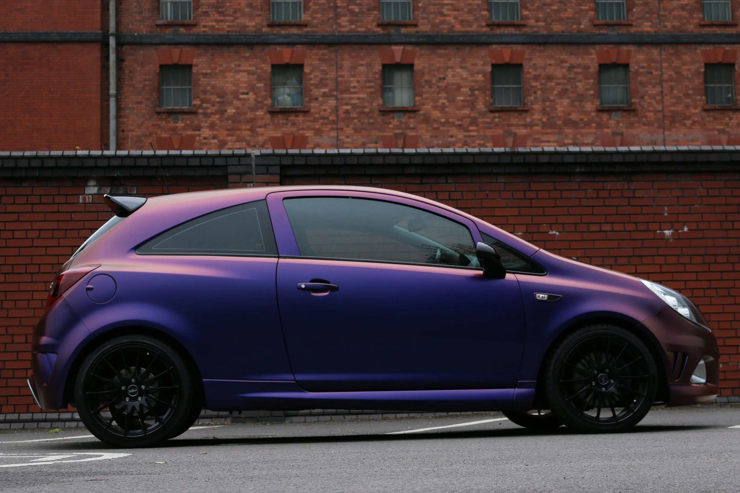 A purple sports car parked on a street in front of a brick wall.