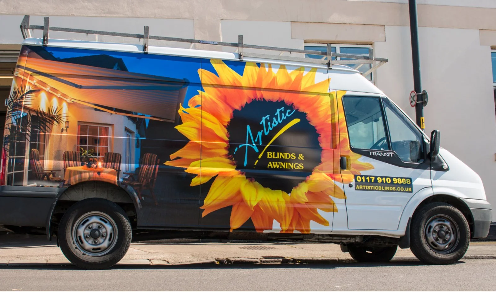 A van with vibrant graphics of a large sunflower and a sunset scene, advertising 'Artistic Blinds & Awnings' with contact information and website.