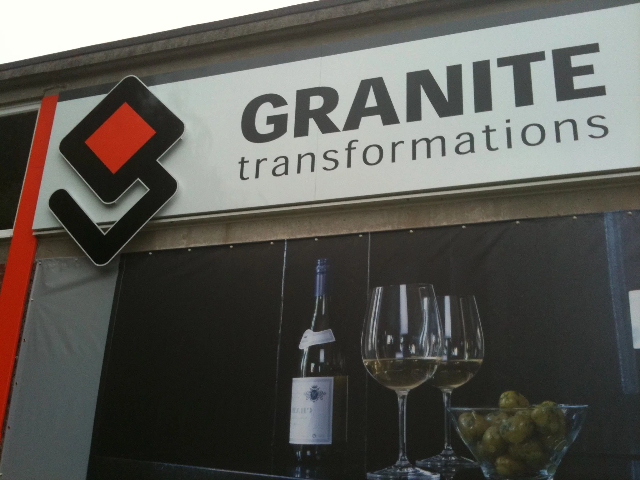 Sign for Grande Transformations with black text and a black and red diamond logo above the text