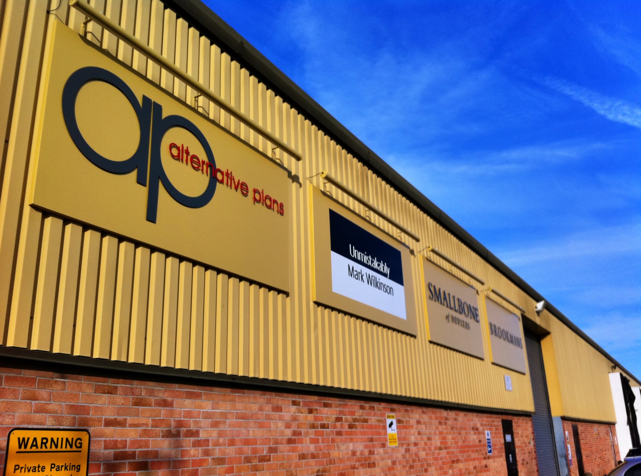 Exterior of a store with a sign that reads "Q HQ alternative plans" and other signage, under a blue sky.