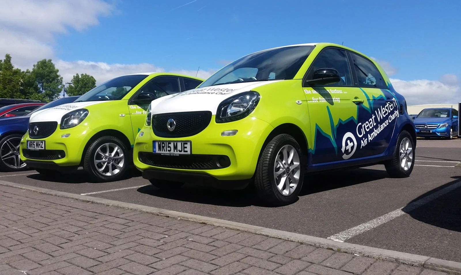 Parking lot with bright green and blue vehicles marked with 'Great Western Air Ambulance' along with logos and slogans.