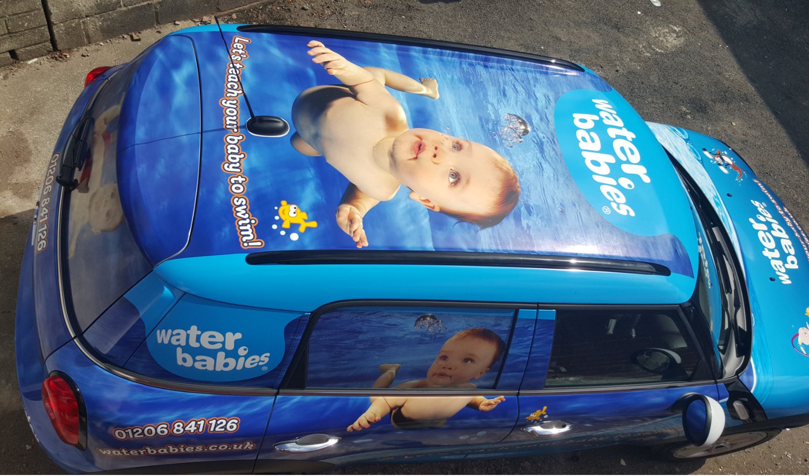 A car with a Water Babies advertisement featuring images of babies swimming underwater with floating toys on a blue background.