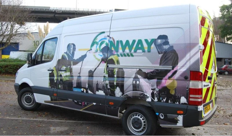 A white van with outdoor advertising wrap featuring silhouettes of workers and the text 'ONWAY'.