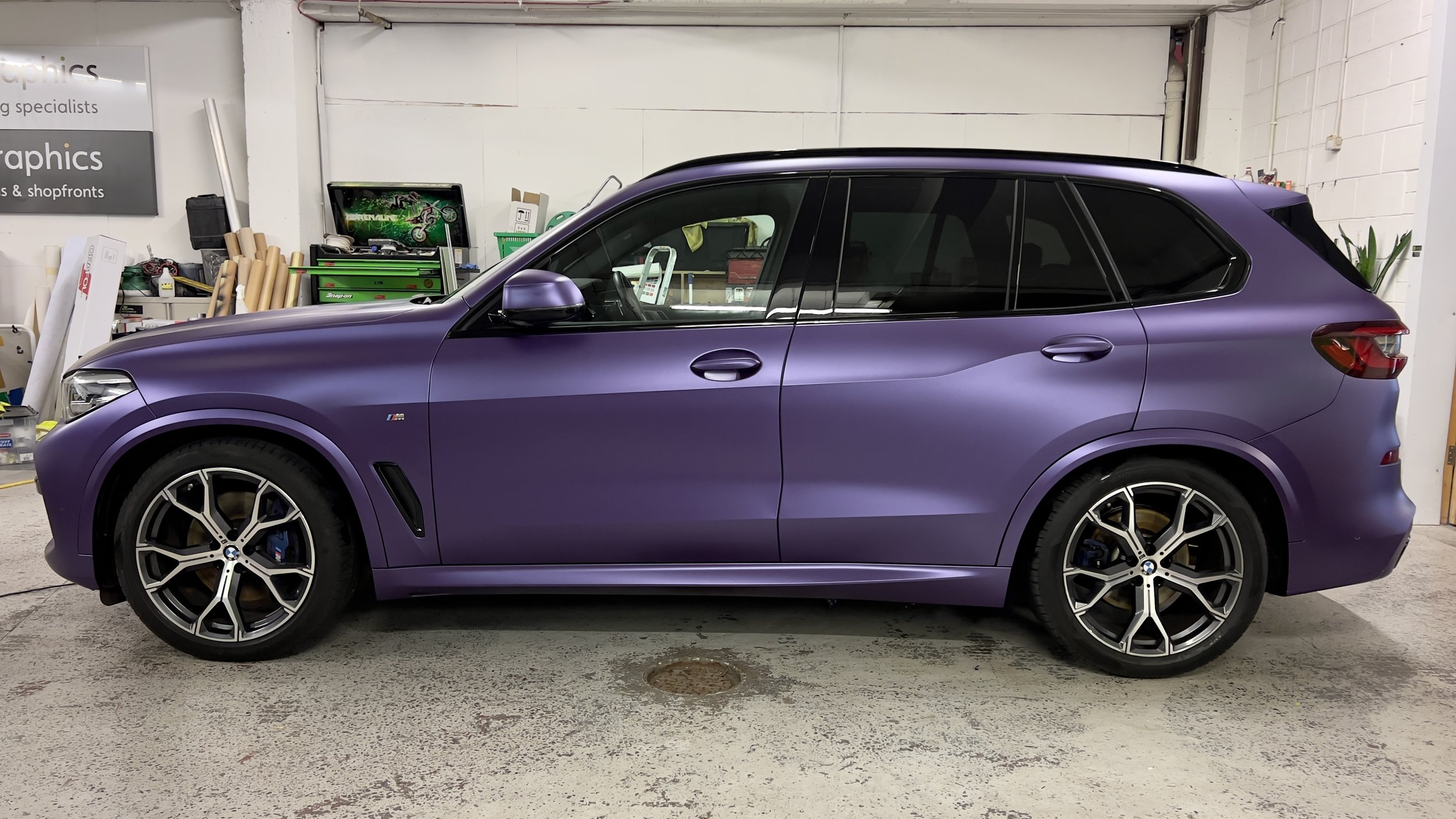 A purple BMW SUV parked inside a garage with a cluttered workbench and various tools in the background.