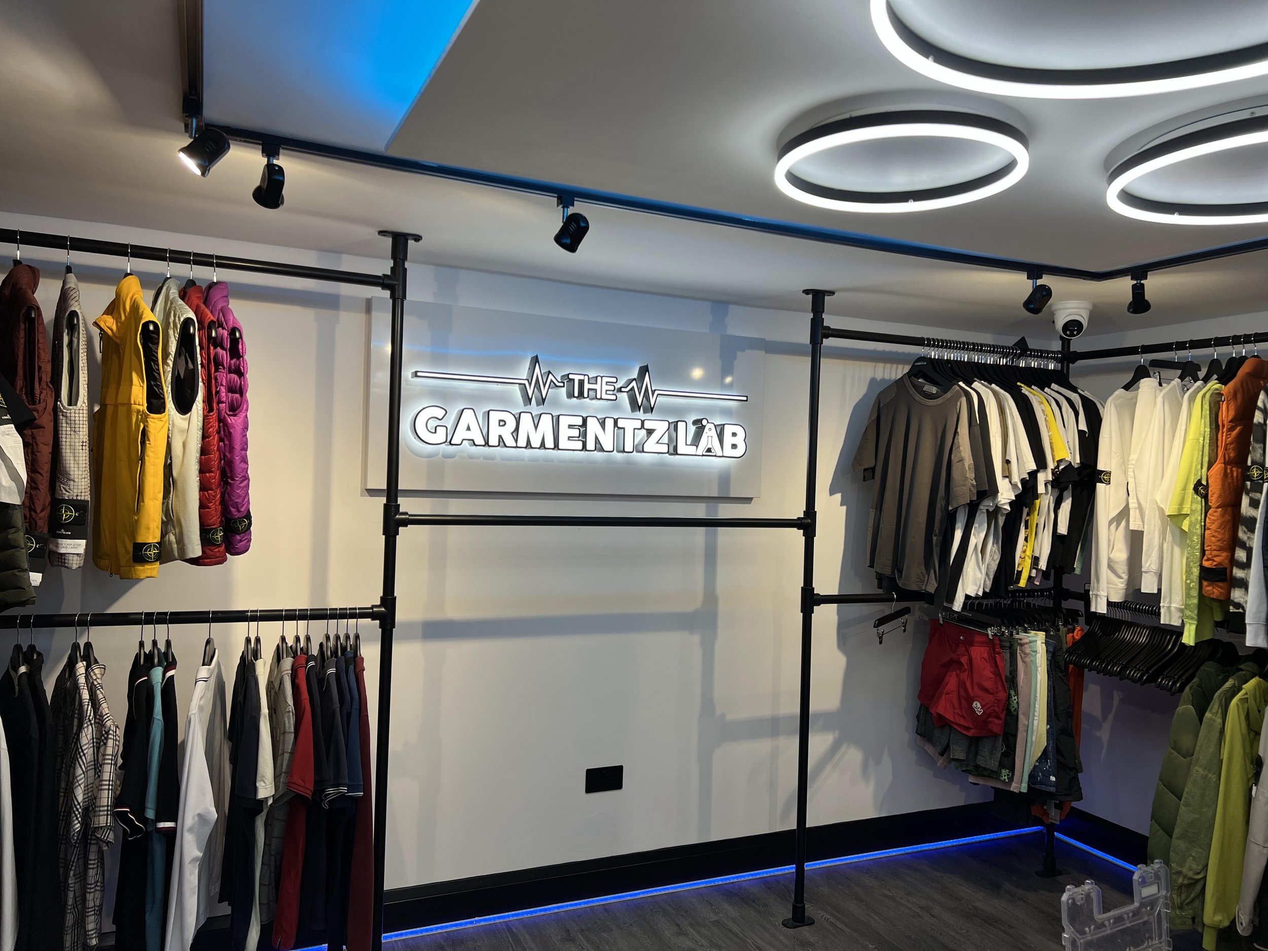 Clothing display inside The Garmentz Lab store with racks of assorted casual and sportswear clothing, illuminated by modern ceiling lights.