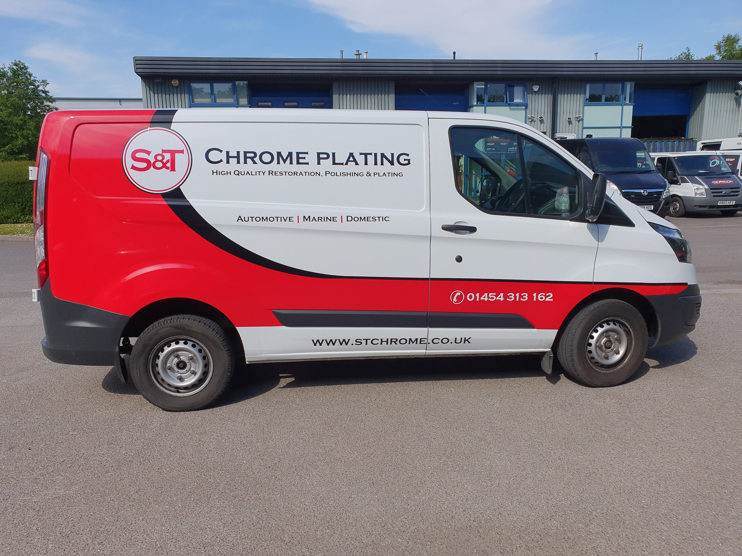 A white and red delivery van parked on a parking lot with a blue industrial building in the background. The van has text indicating it is from S&T Chrome Plating, offering high-quality restoration, polishing, and plating for automotive, marine, and d