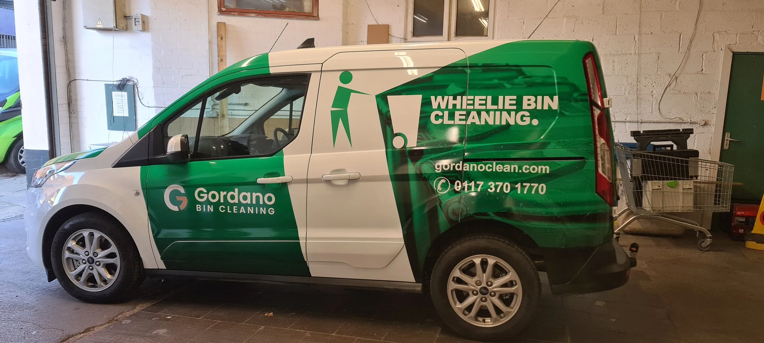 A white and green Gorrdano bin cleaning service van parked inside a garage with a shopping cart nearby.