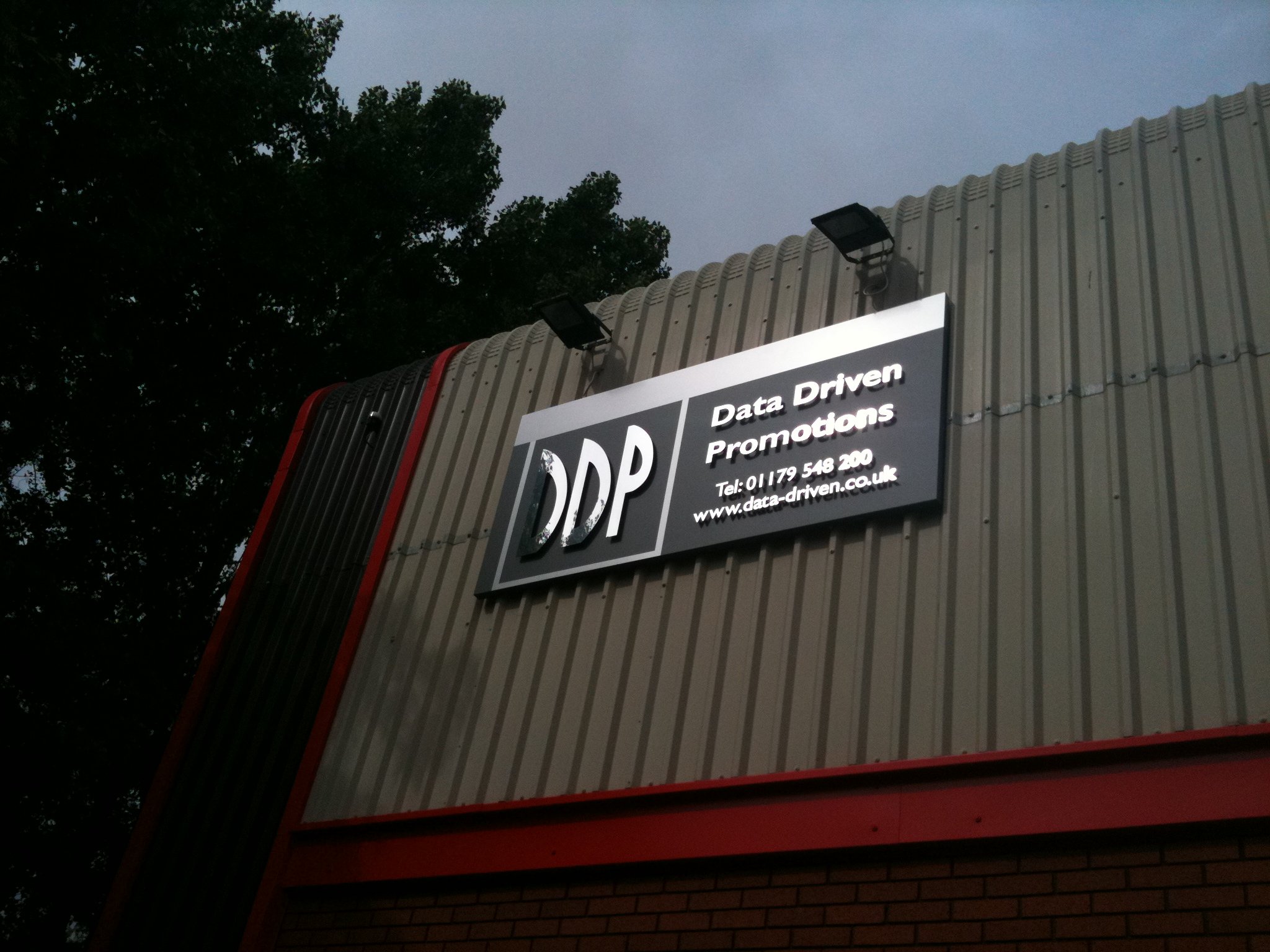 A sign on a building reads, 'Data Driven Promotions' with a phone number and website, and there are two outdoor lights mounted on the building's wall.