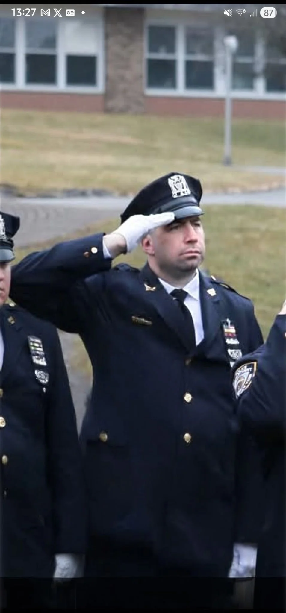 A police officer saluting during a formal ceremony, standing outdoors in a uniform with medals and a police badge.