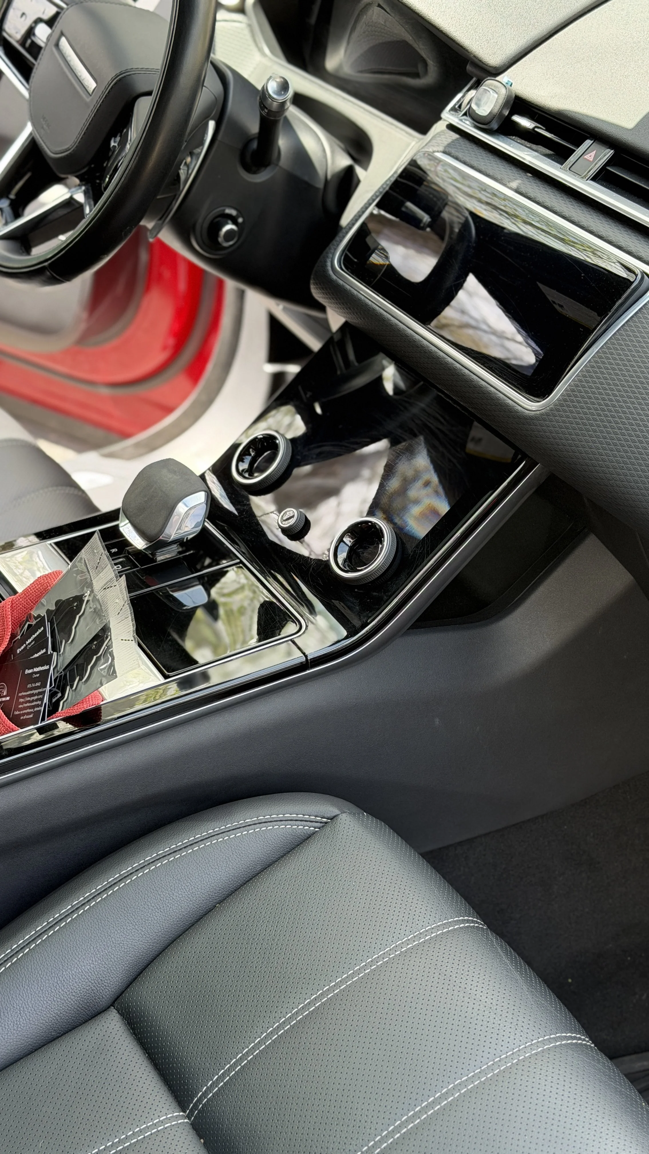 The interior of a modern car showing the dashboard, steering wheel, center console with a large touchscreen, gear shift, and part of the gray leather seat.