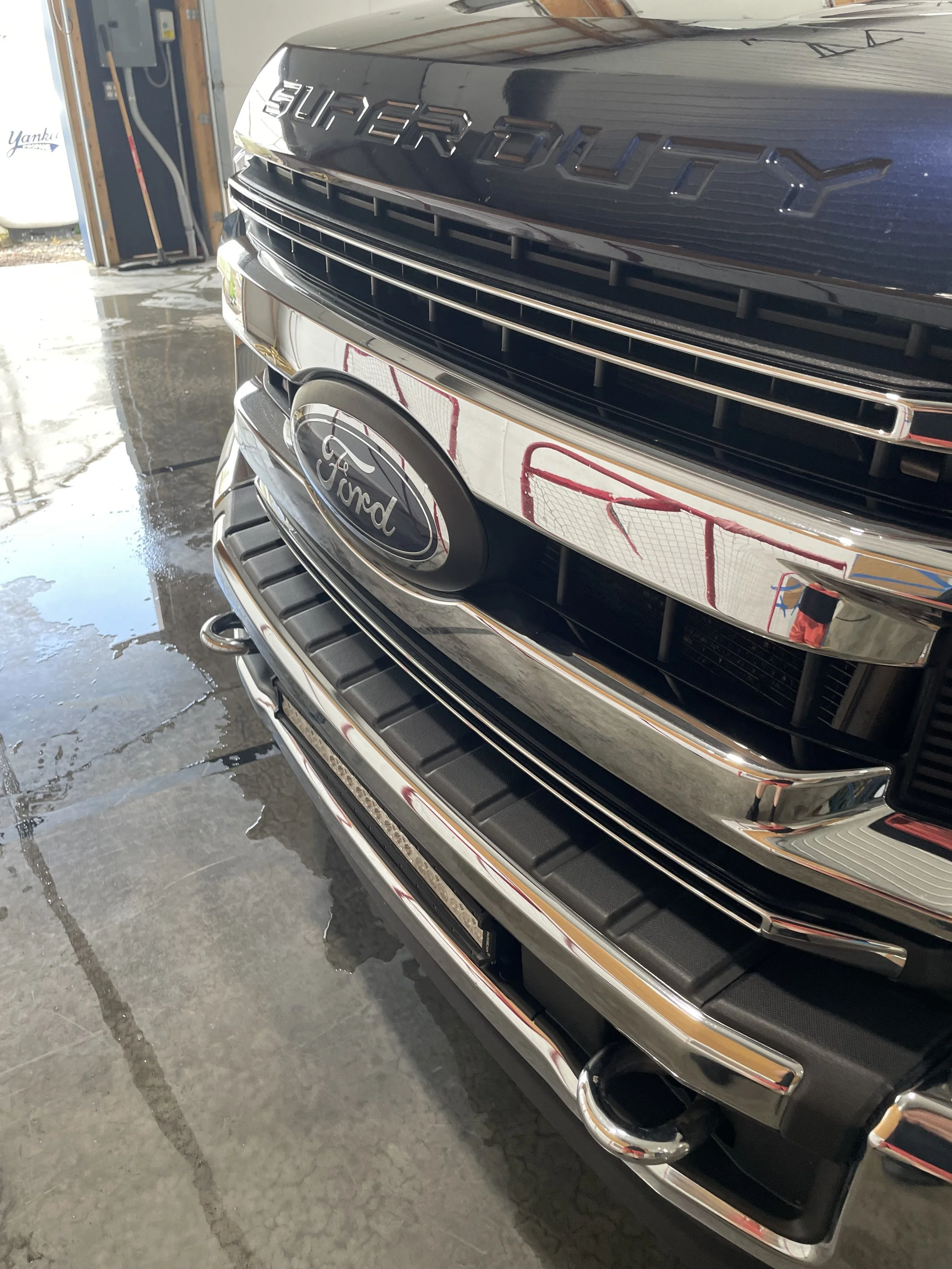Close-up of the front grille and emblem of a black Ford Super Duty truck in a garage.